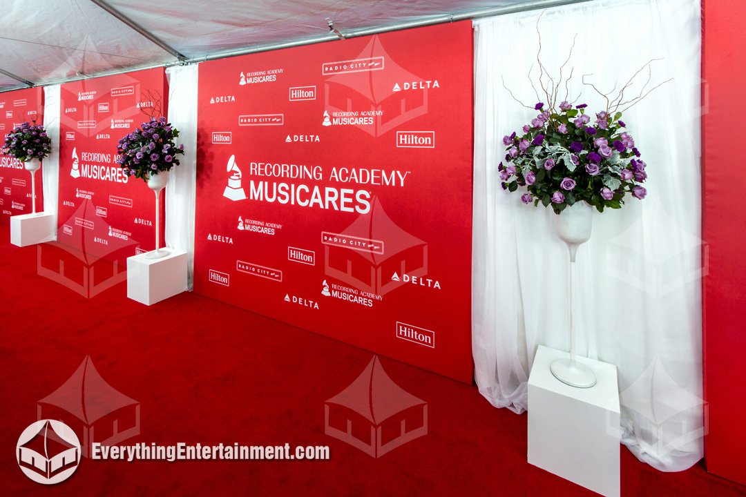 MusiCares branded step and repeat backdrop with floral arrangements and red carpet flooring installed by Everything Entertainment.