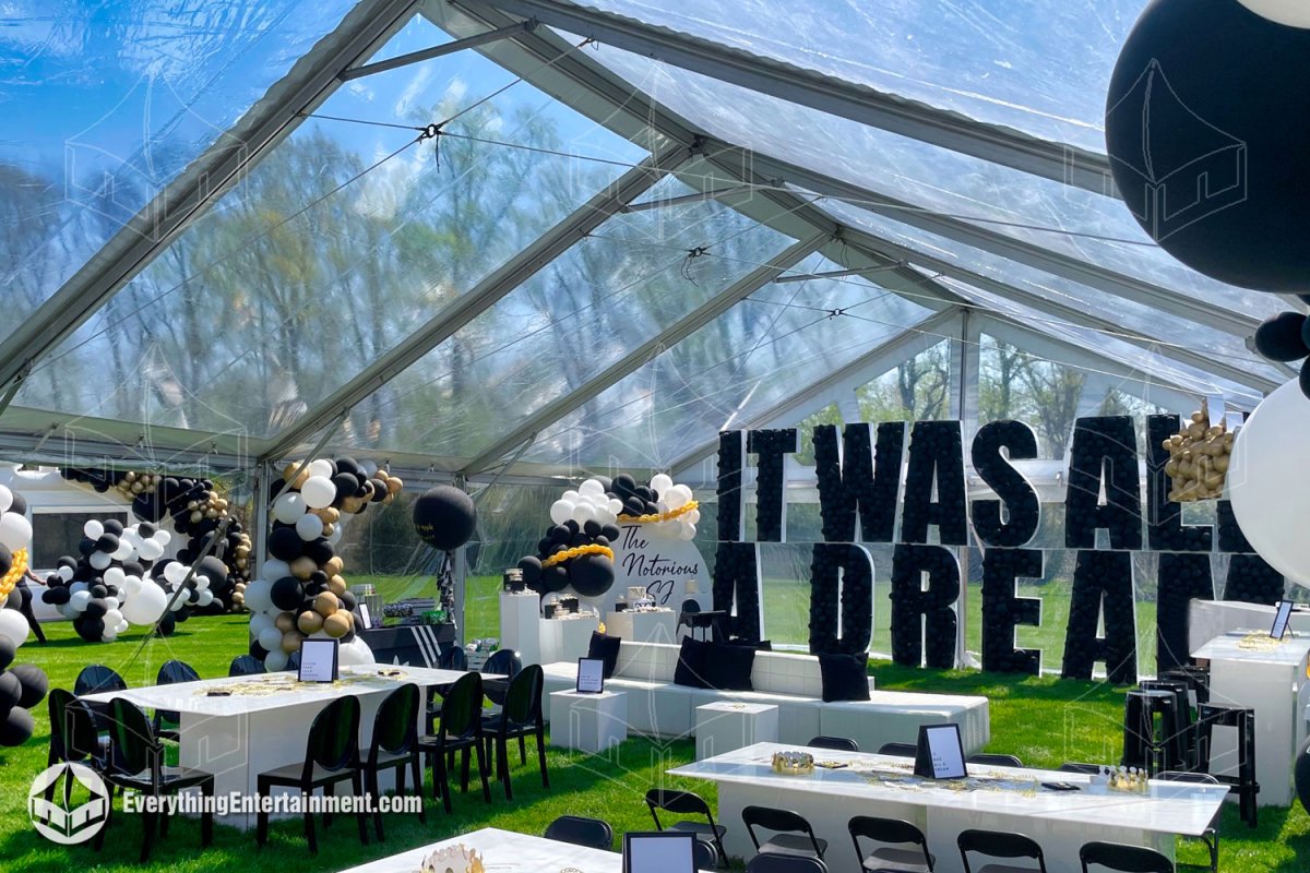 Bright interior view of a 30x50 clear top frame tent with black, white, and gold balloon decor, custom marquee lettering, and modern dining seating set up for a birthday party in Holmdel NJ by Everything Entertainment.