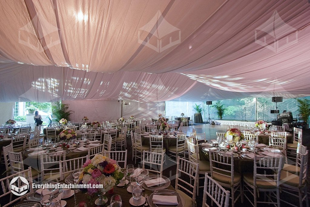 Interior view of a 40x90 wedding tent in Manalapan NJ featuring a pleated white liner lit in pink, gobo breakup projections, ballroom chairs, round dining tables, and a band stage built on a cantilevered subfloor by Everything Entertainment.