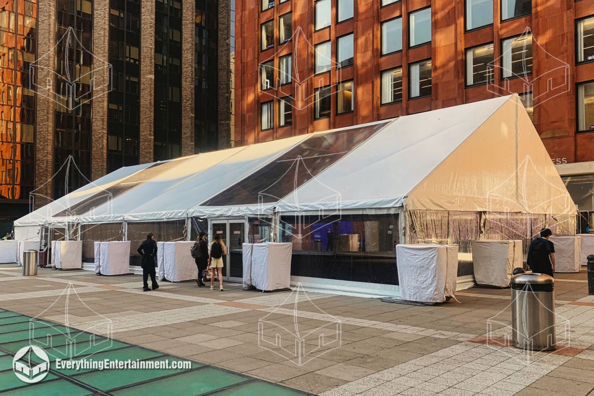 Exterior view of a 50x90 frame tent with alternating clear and white top roof panels, glass entry doors, and concrete ballasts installed on a floating tile plaza at NYU Stern by Everything Entertainment.