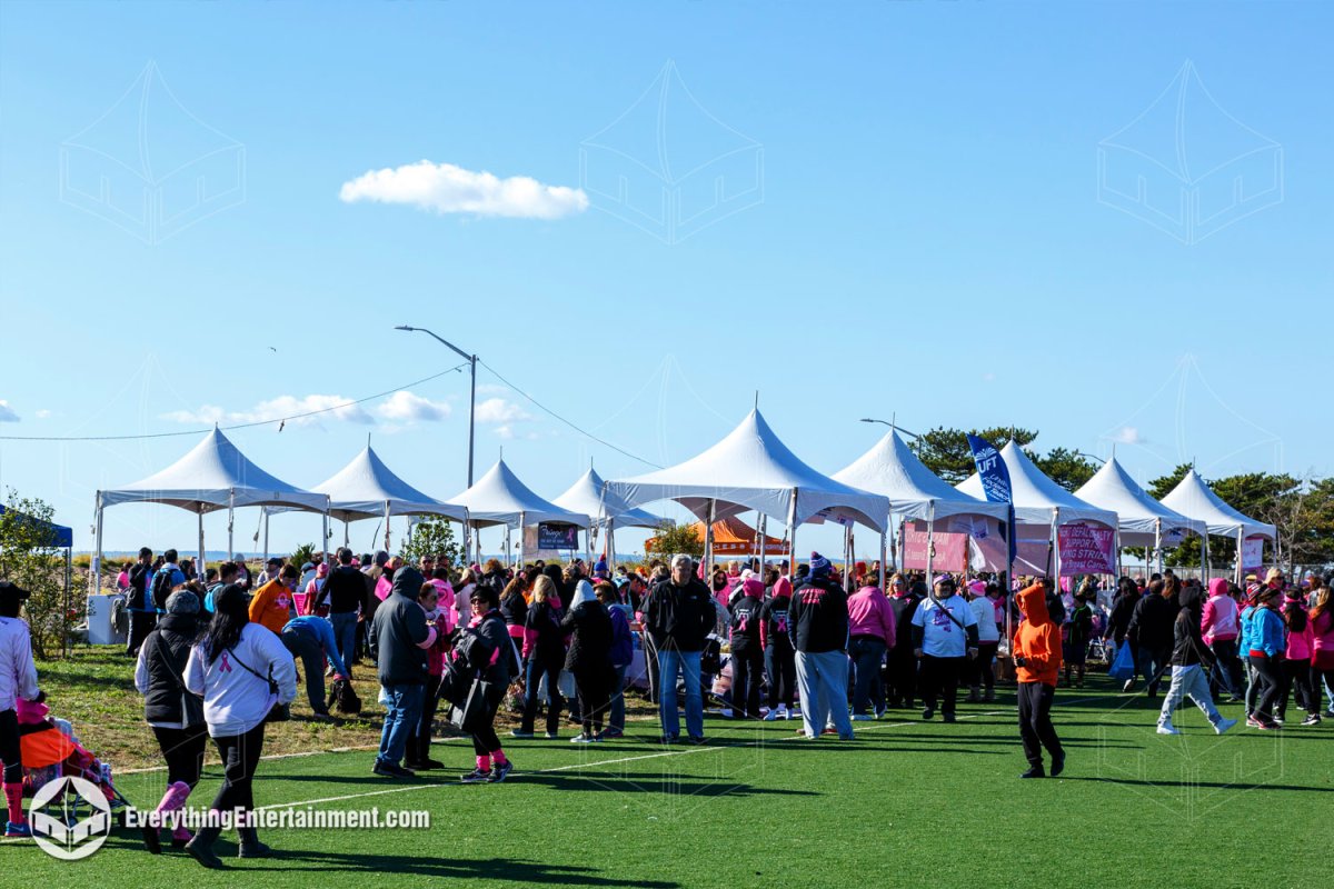 Crowd of walk participants gathered around a village of white high peak tents on a turf field on Staten Island by Everything Entertainment.