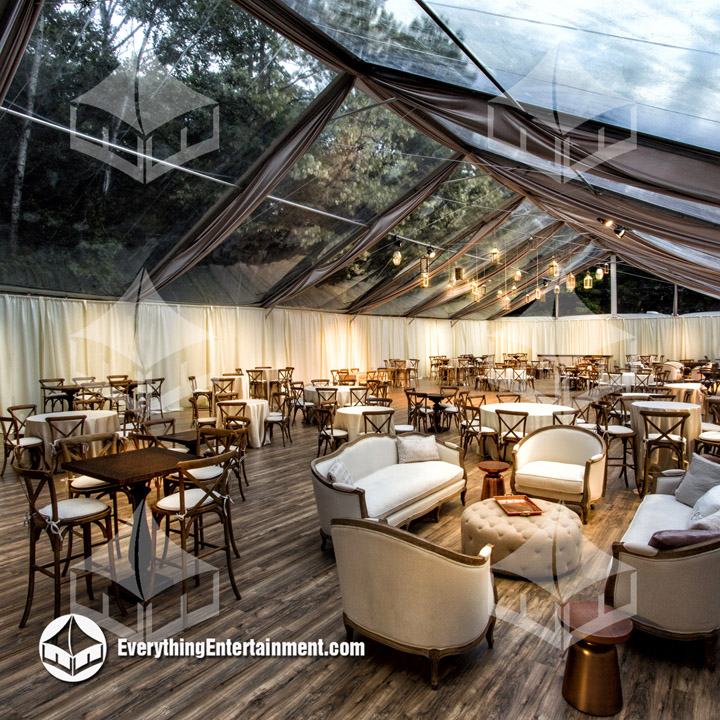 Huge clear top tent with rustic party rentals setup on a hardwood floor.