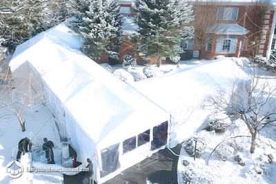 Climate-controlled white frame tent installed beside a brick mansion during a heavy snowfall, with cable inspections and crew preparing the entrance in New Jersey winter