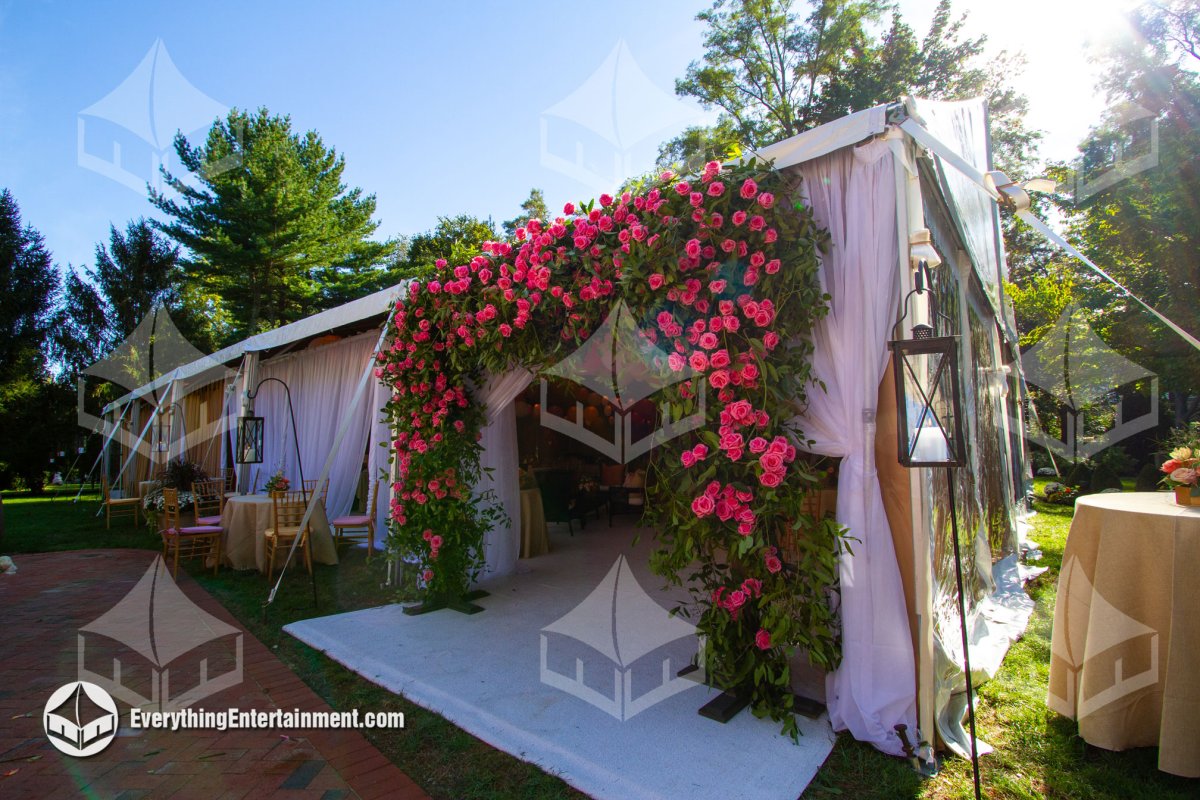 White tent entrance adorned with a vibrant pink rose floral arch, white drapery, and lantern posts set up by Everything Entertainment in Colts Neck NJ.
