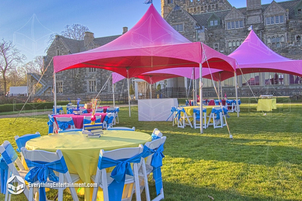 A festive outdoor event setup for Easter and Passover featuring high-peak pink tents on a sunny lawn. Tables are draped in yellow and magenta linens with white chairs and blue sashes, set against the backdrop of a historic stone estate.