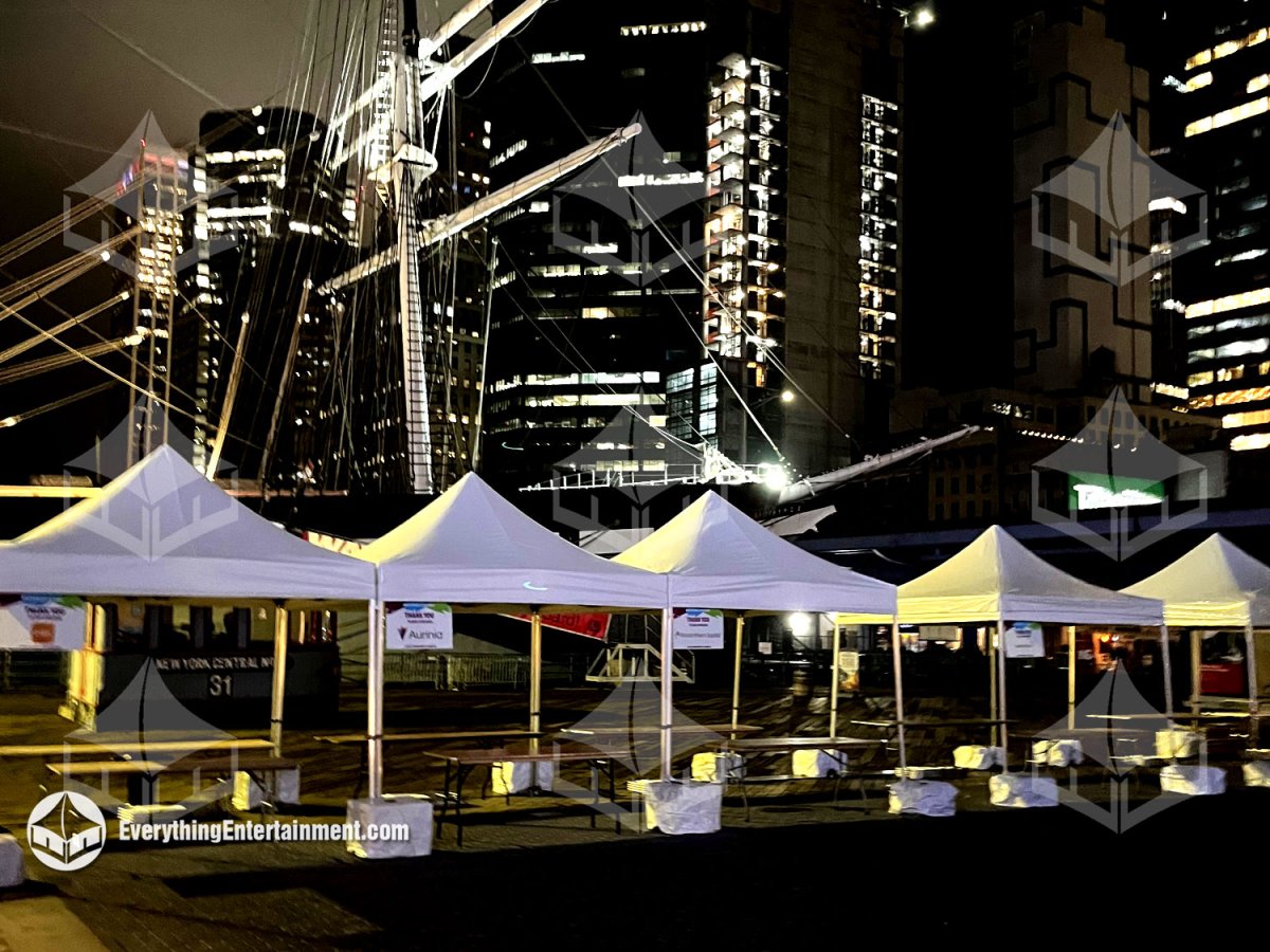 Row of 10x10 high-peak festival tents ballasted with concrete weights set up at night along the Pier 16 boardwalk in NYC by Everything Entertainment.