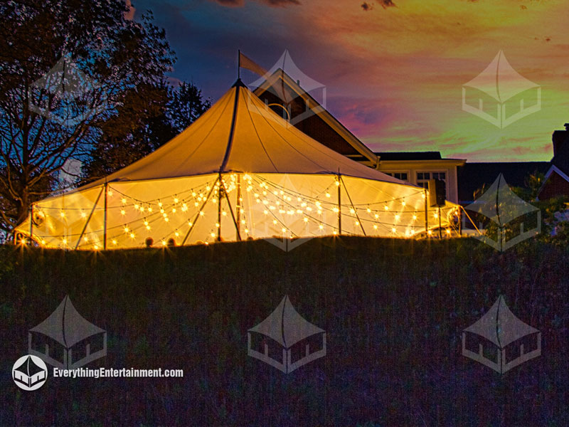 Sailcloth tent in backyard at night with bistro string lights throughout tent.