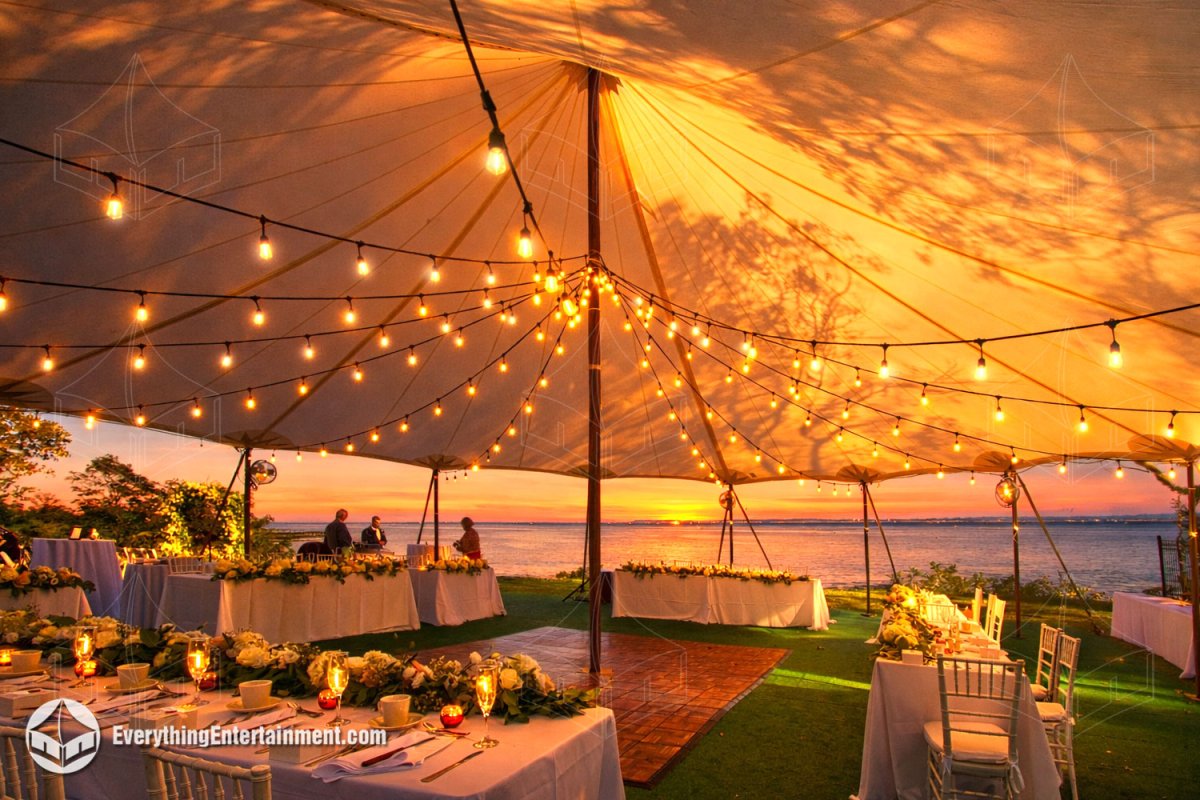 Interior of a sailcloth wedding tent with bistro lights, dance floor, and carpeted subfloor at sunset on Staten Island by Everything Entertainment.