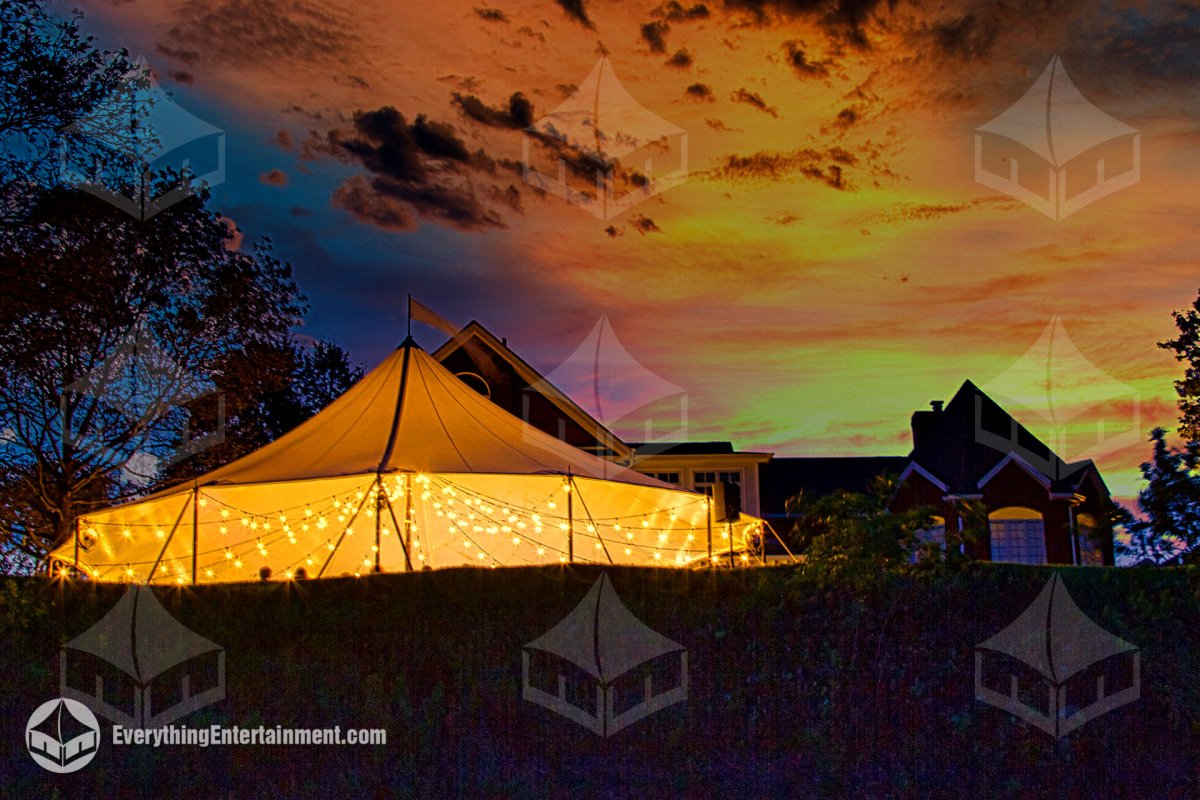 Exterior view of a glowing sailcloth wedding tent illuminated by string lights at dusk on Staten Island by Everything Entertainment.