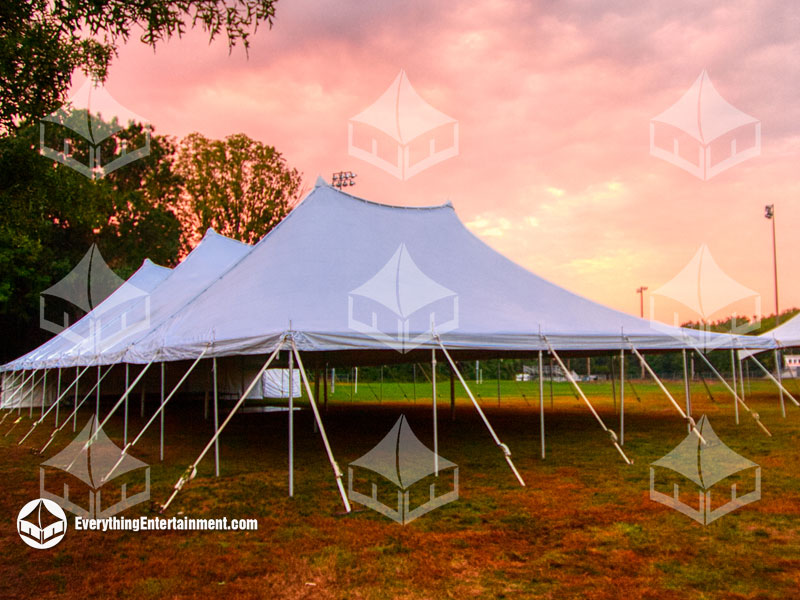 large 60x120 foot white tension tent setup on a field with a orange sunrise