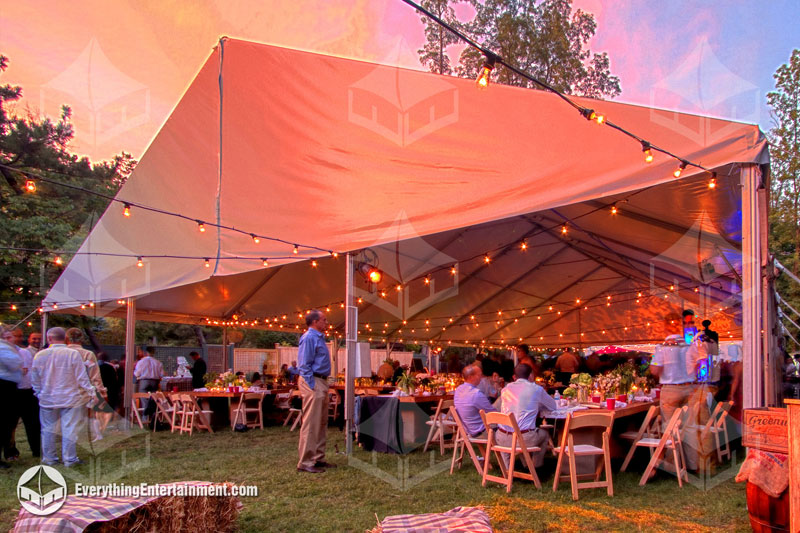 Large white tent setup on grass with string lights and people