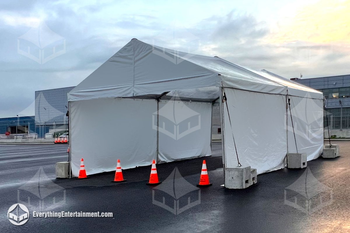 A 20x30 white drive-through frame tent ballasted with concrete blocks and safety cones on an asphalt lot by Everything Entertainment.