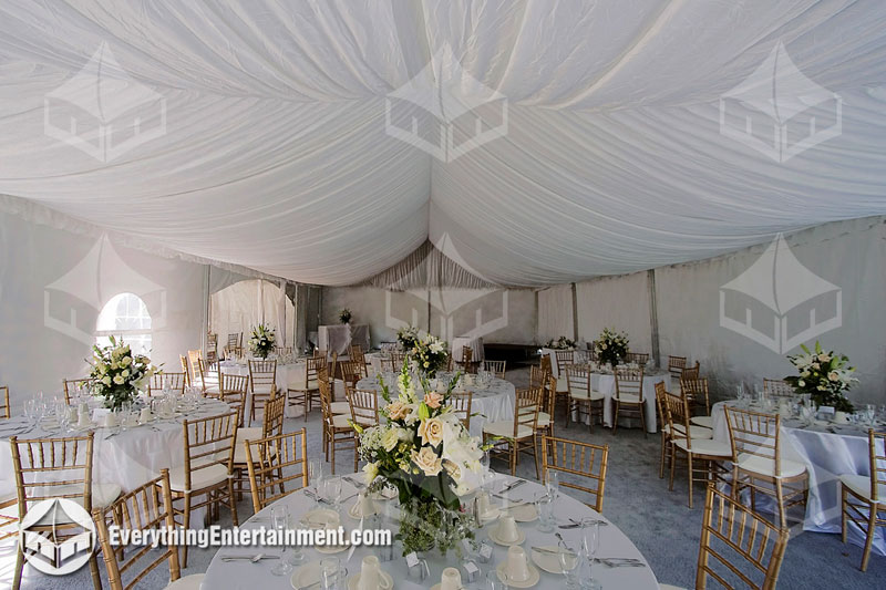 Large tent with white drapery, tables with linens, and silver Chivalri ballroom chairs