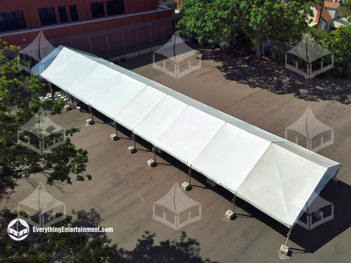 Aerial view of a long white frame tent anchored with concrete ballast blocks on a school asphalt yard for graduation rentals by Everything Entertainment.